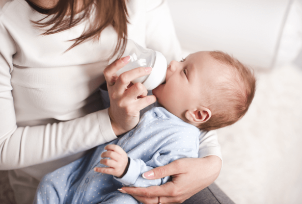 Baby feeding from a bottle in their Monther's arms